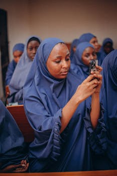 Group of women in blue hijabs using smartphones in a classroom setting.