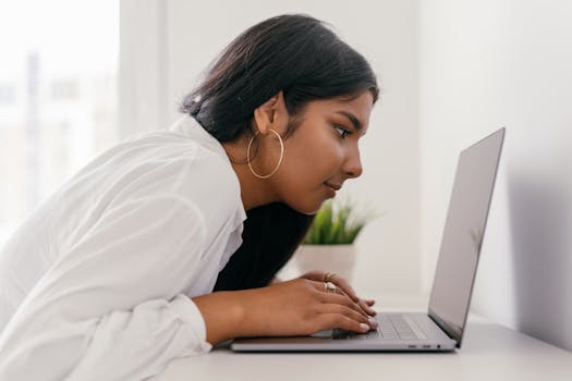 Young woman using laptop for studying, displaying focused expression and engaged posture.